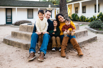 Happy family with three young boys sit on steps outside California adobe