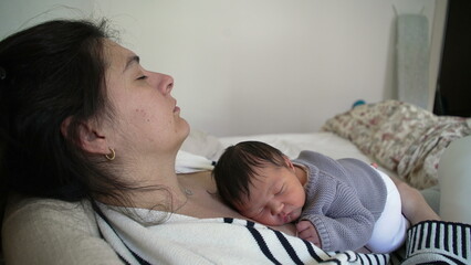 Exhausted mother asleep while holding newborn baby resting on mother's chest in deep sleep slumber, maternal bonding moment between infant and parent during first day life