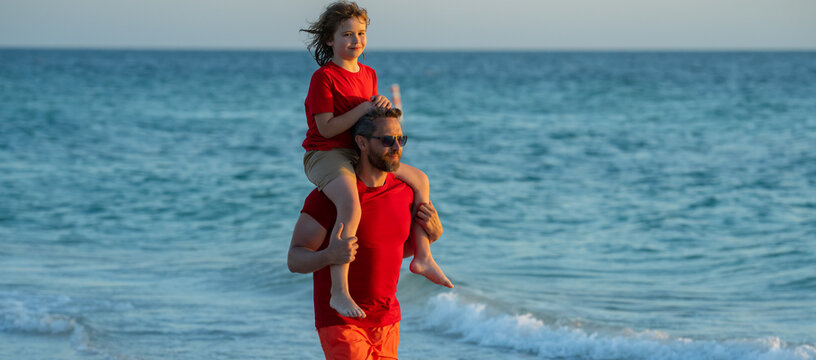 Fathers day. Father walking with a little child son on beach near sea. Dad with son walking on a summer beach. Son on fathers shoulders piggyback ride. Summer holiday, vacation with father.