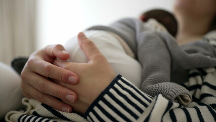 Close-up of mother hands holding newborn baby infant close to her chest while napping, detail of...