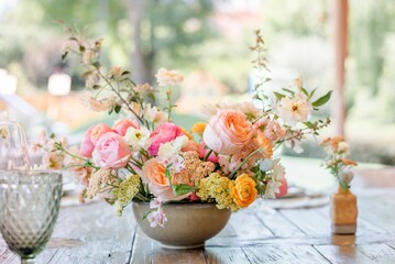 a bowl with many different colored flowers on a table next to wine glasses