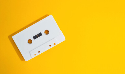 A white cassette tape is laying on a yellow surface