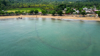 Big fishing net floats in the water near a sandy beach in Praia Grande, Sao Tome, South Africa