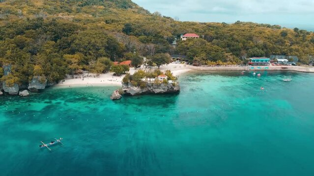 Drone over the sea revealing Salagdoong Beach with greenery under cloudy sky in Philippines