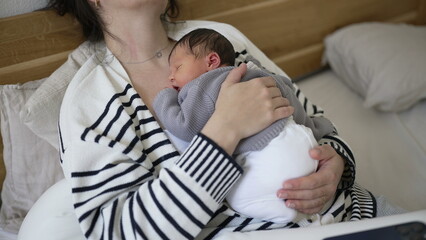 Mother holding sleeping newborn baby close to chest held with love and care during afternoon nap...