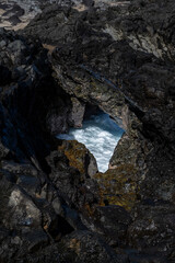View down into rocky black lava rock blow hole at Pacific Ocean foam in a sunbeam, , Makalua-Puna Point, Maui, Hawaii, as a nature background
