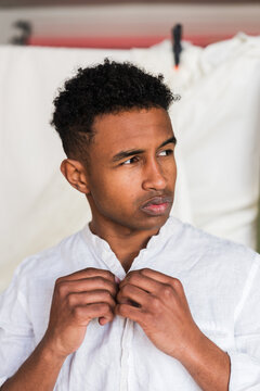 Young man buttoning white shirt with concerned expression