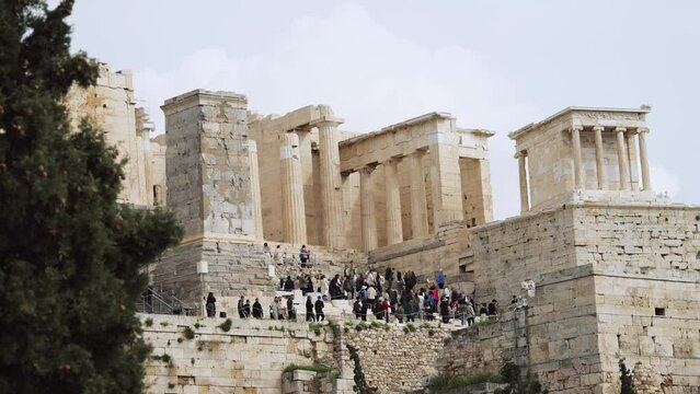 Crowd of tourist people walk at entrance of Acropolis visiting the Monument of Agrippa and Temple of Athena Nike