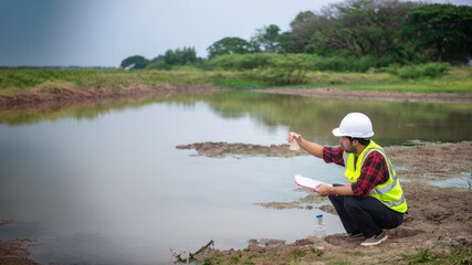 Environmental engineer Sit down next to a well and raise the glass tube that full of water sample to analysing check the quality and contaminants in the water source.