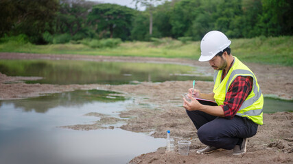Environmental engineer Sit down next to a well and take note while holding the glass tube in his left hand to analysing check the quality and contaminants in the water source.