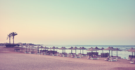A tranquil beach with sun loungers and umbrellas at sunset, color toning applied, Egypt.
