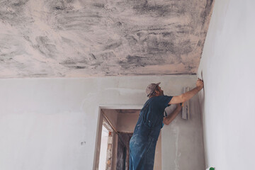 Man plastering the walls with finishing putty in the room with putty knife or spatula. Repair work, decoration building concept, construction.