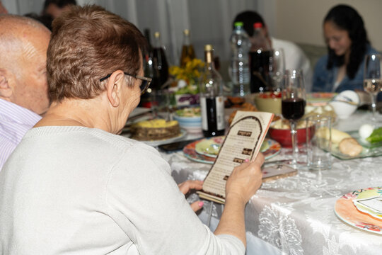 Senior Woman With Passover Haggadah At Seder.Family,Food In Background