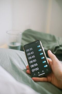 A man's hand holds a smartphone with the alarm clock on. POV style. 