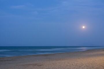 Close-up of Gandia beach with moonrise in the background of the photo.