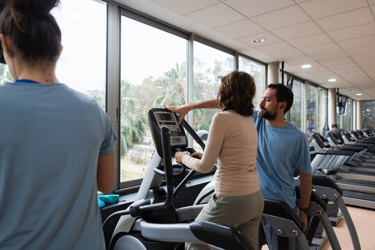 Personal trainer assisting man on gym elliptical machine