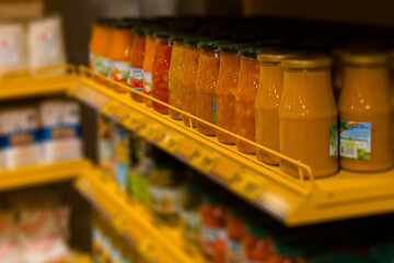 In the store, a yellow shelf displays jars of various food items for sale