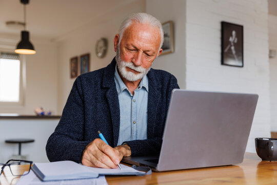 Senior businessman writing in notebook at desk