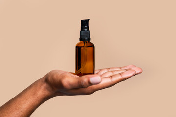 Hand holding amber spray bottle isolated on neutral background