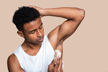 Young adult male carefully applying stick deodorant on his underarm
