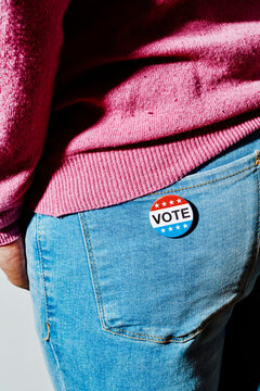 man stands weargin a vote badge in the back pocket of his jeans