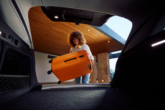 Young woman puts a suitcase in the trunk