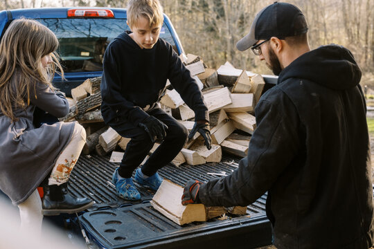 young family man and his children stacking firewood in spring