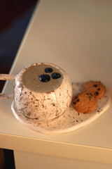 Cup of blueberry and banana smoothie and chocolate chip cookies on the table, illuminated by sunlight. Selective focus.