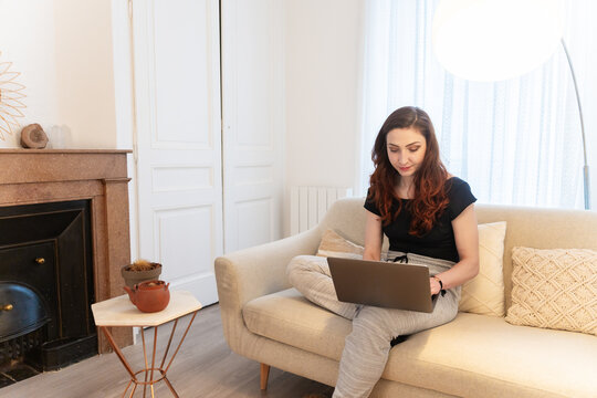 Woman Sitting On The Couch With A Laptop On Her Bedroom.