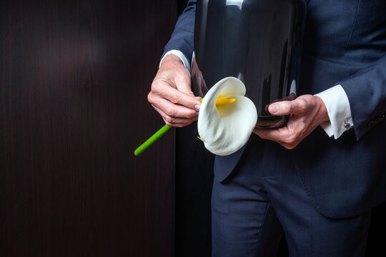 Mourning man in crematorium with cremation urn with ashes and flower at burial or funeral. Copy space.