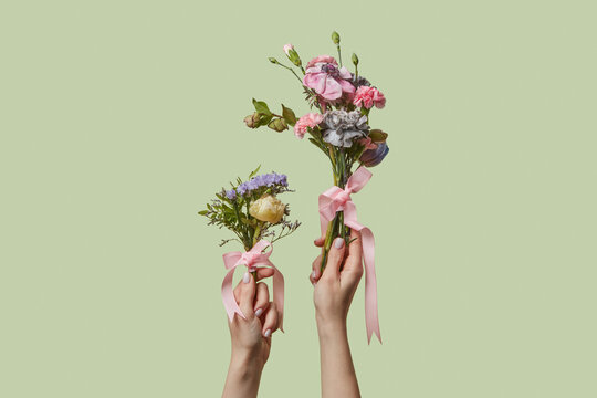 Hands holding bouquets tied with pink ribbon on green background