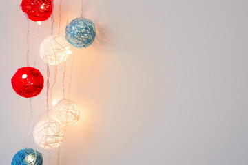 Red white and blue string lights made from yarn with light strings hanging off them. House decoration in honor of Independence Day or Memorial Day. American patriotic theme. 4th Of July background..