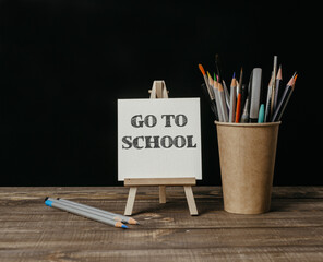 A wooden desk with a white sign that says Go to School and a cup of pencils