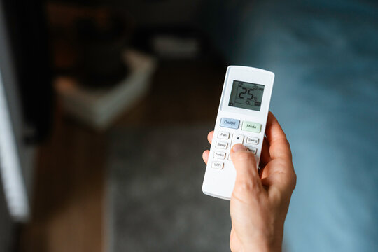 The woman controls the air conditioner using the remote control