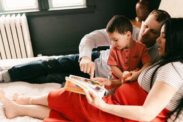 parents (incl pregnant mom)  reading to toddler on bed