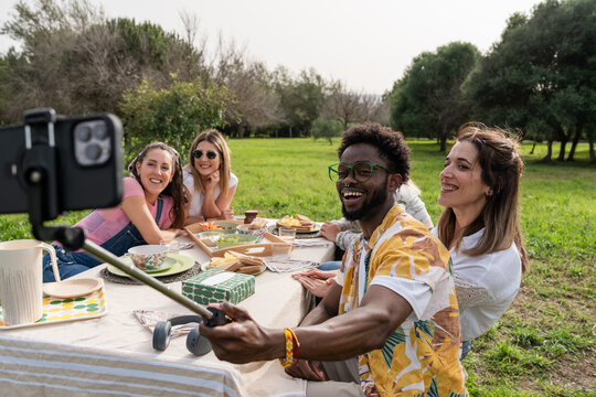 Friends enjoying picnic and taking selfie in park