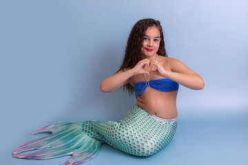A pretty child girl in a mermaid costume, sitting on a blue background