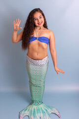 Beautiful smiling girl in a mermaid costume, friendly, standing on a blue background