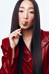 Young woman with long black hair and red jacket enjoying a lollipop while looking into the distance