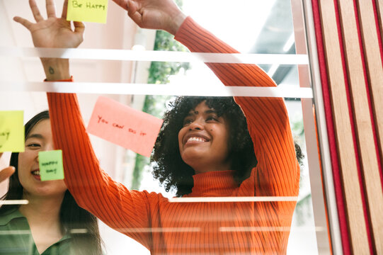 Casual businesswomen smiles while placing sticky notes on glass