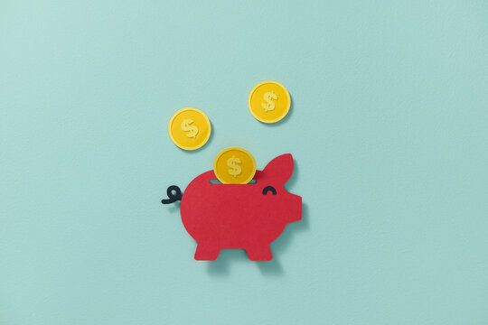 Lots of cent coins flying into a red piggy bank cut from paper