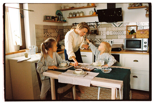 Mother and her two adorable daughters eating in the kitchen together