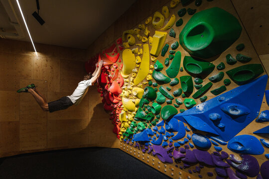 Skilled climber bouldering on a rainbow colored overhang climbing wall