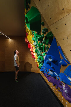 Young climber looking at a rainbow colored  overhang climbing wall