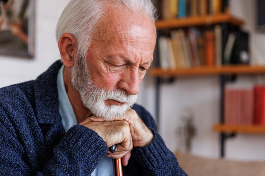 Sad senior man leaning on cane at home