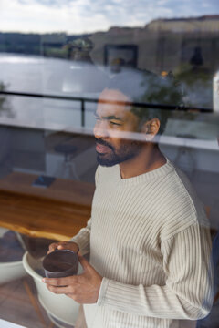 Thoughtful man looking through window glass