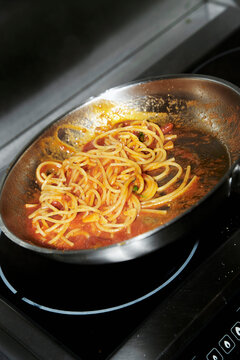The pasta in the tomato sauce in the pan is stirred together 