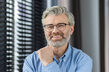 Confident and happy elderly man with grey hair and glasses smiling in a modern office setting