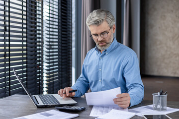 Focused professional businessman working on financial documents in a modern office setting