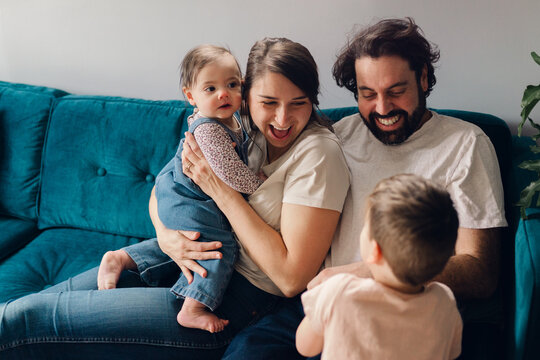happy family with baby girl and little boy hugging on sofa 